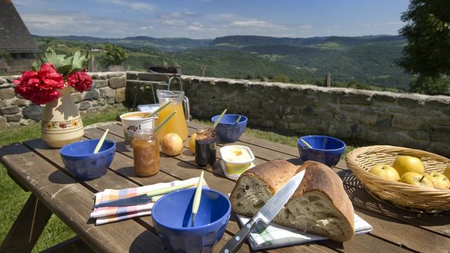 Petit déjeuner en terrasse d'un gîte sur l'Aubrac avec des produits locaux Pain, miel, confiture, fruits ... et une belle vue panoramique