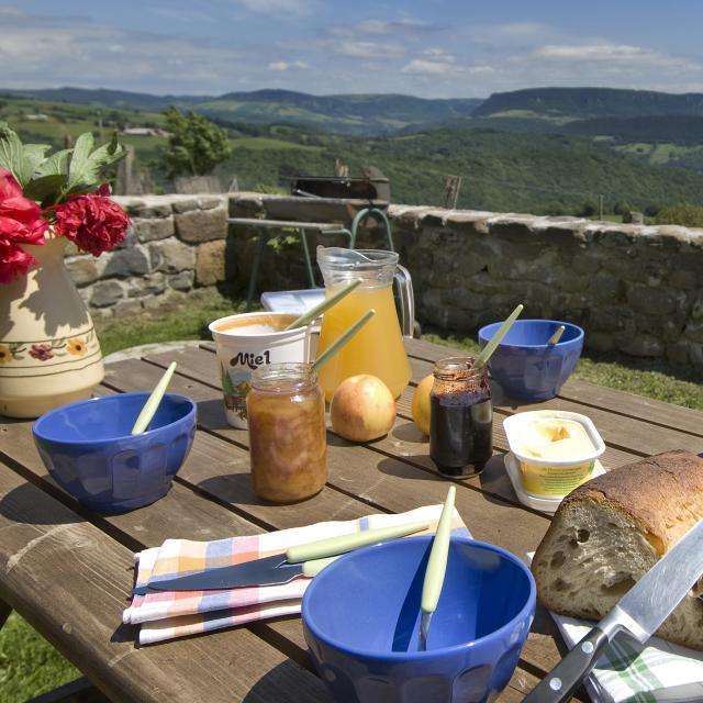 Petit déjeuner en terrasse d'un gîte sur l'Aubrac avec des produits locaux Pain, miel, confiture, fruits ... et une belle vue panoramique